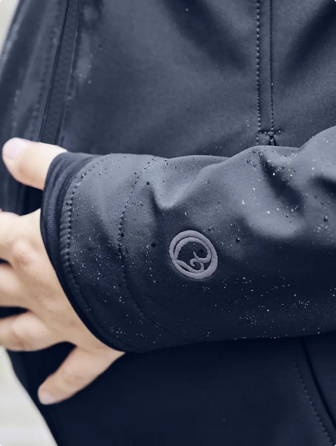 Eine Frau in schwarzer Tragejacke hält sich den schwangeren Bauch.